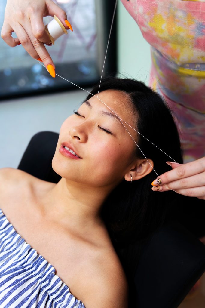 beautician performs eyebrow threading on a woman